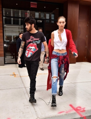 Với phong cách punk-rock, Gigi Hadid chọn cho mình áo tank top cộc tay mix cùng jeans rách và boots hầm hố không quên thắt eo kiểu áo sơ mi cùng áo cardigan đỏ dài bên ngoài. Anh bạn trai chọn set đồ đen với áo thun The Rolling Stones – kiểu áo rất được ưa chuộng 1 thời