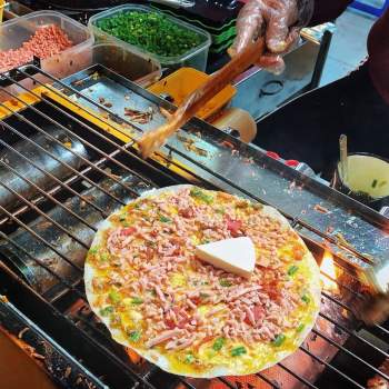 Bánh tráng nướng là món ăn đường phố phổ biển ở Đà Lạt, được ví như pizza của Việt Nam. Bánh tráng nướng trên bếp than, kết hợp với các topping phong phú như ruốc, phô mai, bò khô, hành phi, mỡ hành, tương ớt... Vị đậm đà, béo thơm của các loại nhân hòa quyện, kết hợp với lớp vỏ giòn nóng hổi, tạo nên những chiếc pizza hấp dẫn thực khách bốn phương. Ảnh: Normaltus.