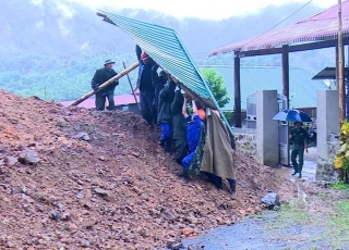 Lực lượng chức năng và người dân di dời mái tôn nhà ra khỏi khu vực sạt lở núi. Ảnh: TTXVN.